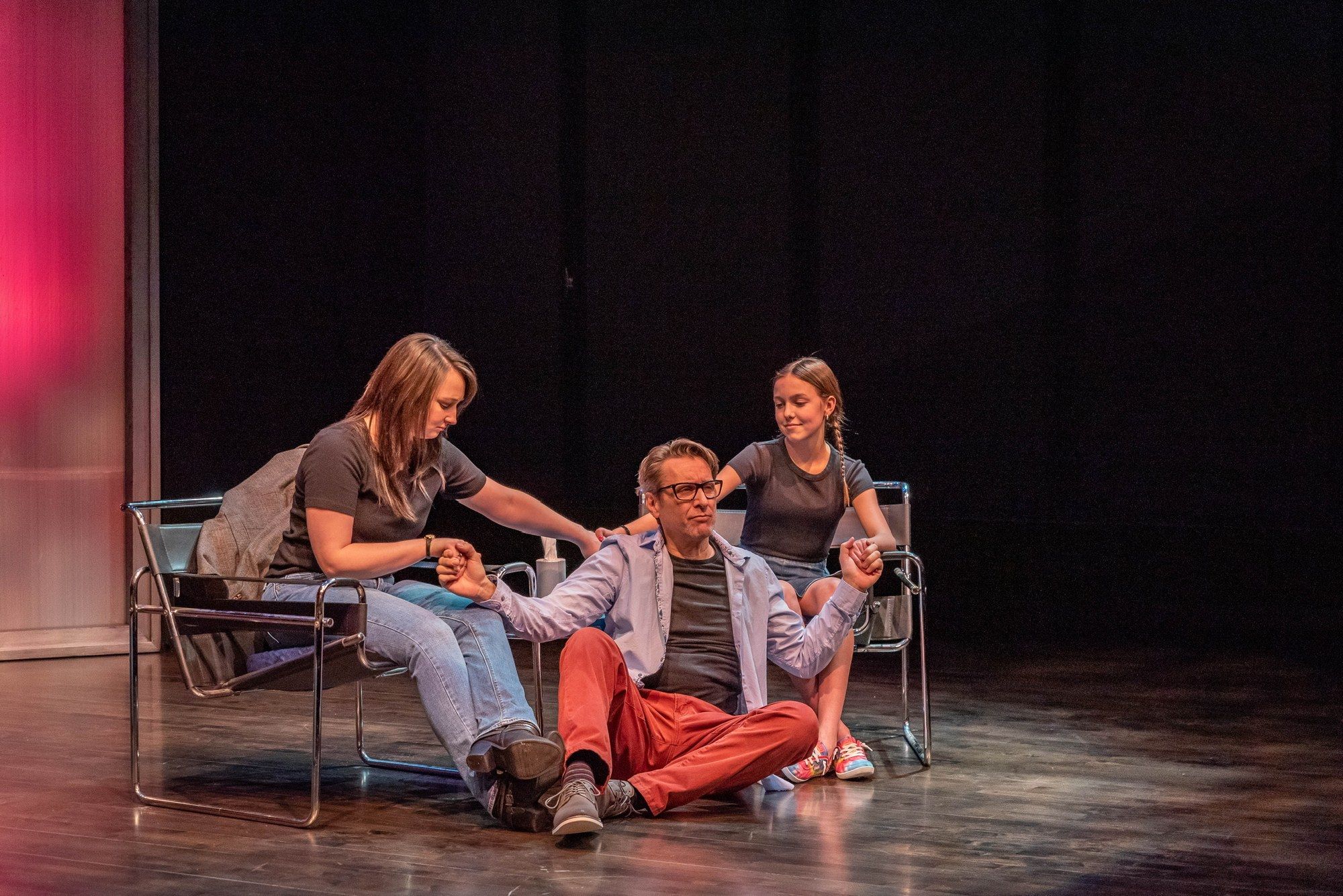 Two women and a girl with a long braid seated around a man on the floor, all holding hands, in Jake's Women at Moonstone Theatre