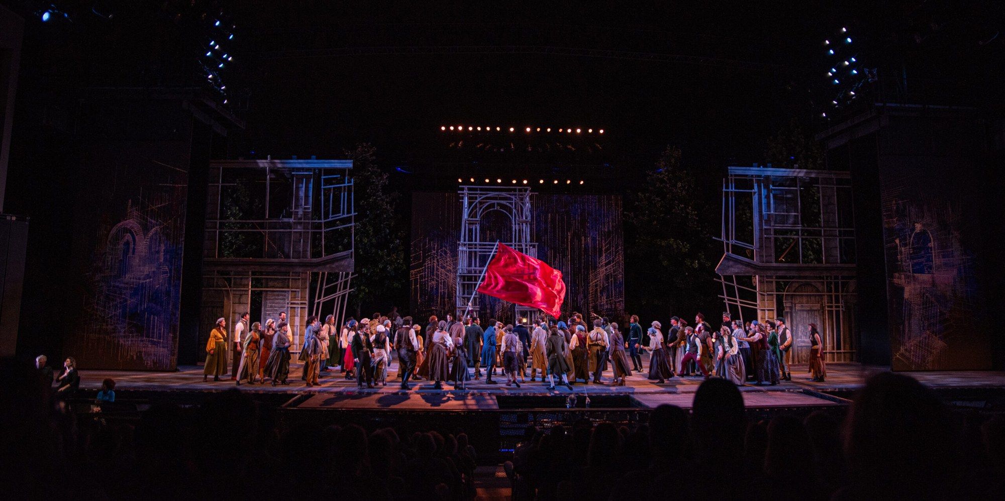 The full company gathered on a barricade set beneath a large red flag in Les Misérables at The Muny