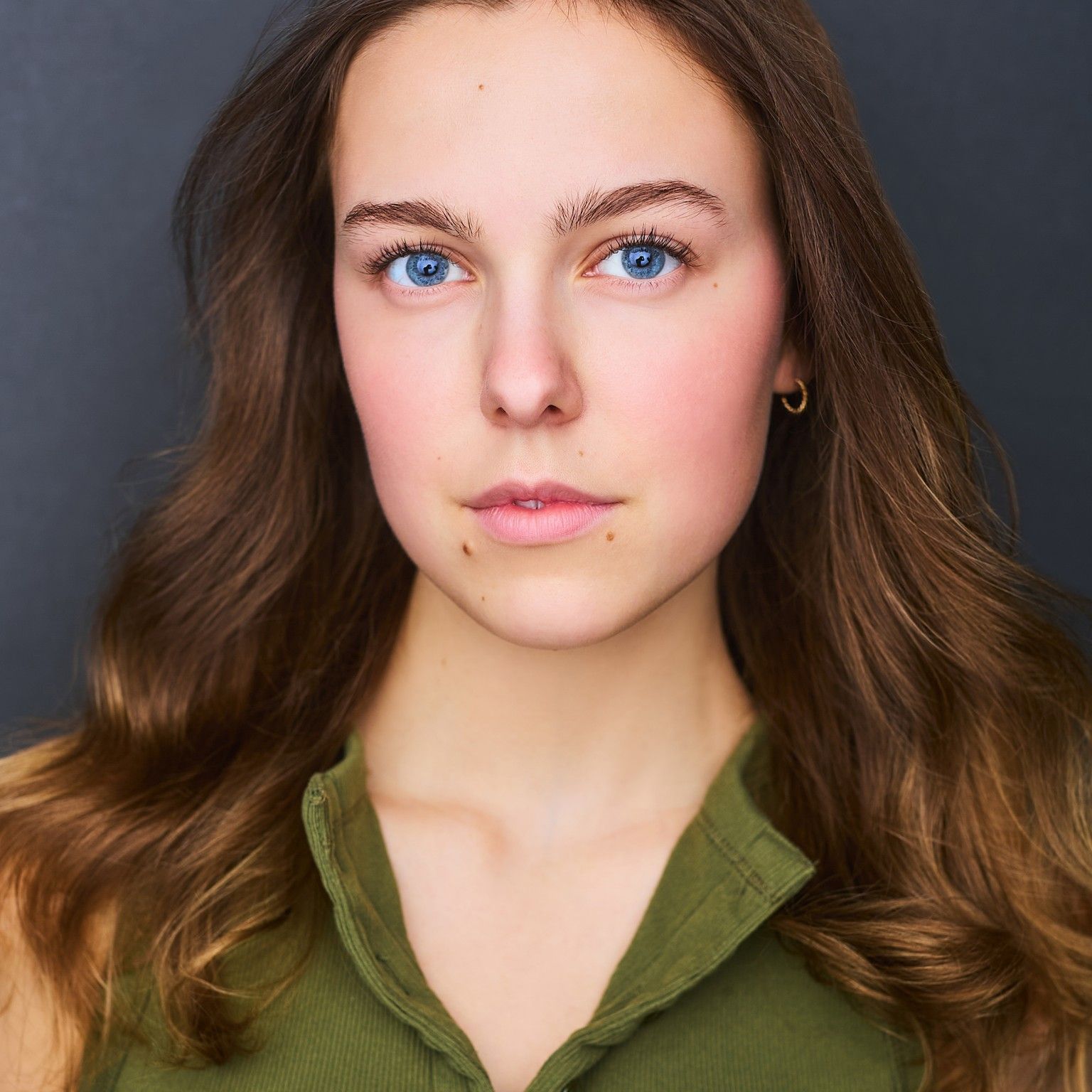 Amelie Lock in an olive top, close studio headshot, a calm direct look into the camera, against a dark backdrop