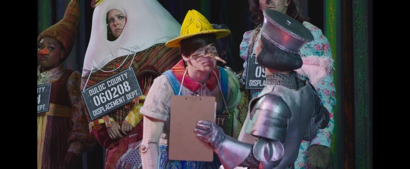 Fairy-tale characters in costume wearing Duloc County displacement department number tags, in Shrek The Musical