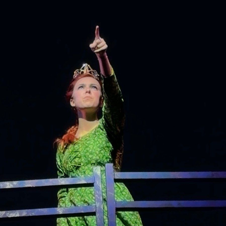 Amelie Lock as Teen Fiona in a green gown and crown, pointing to the sky, Shrek The Musical at The Muny
