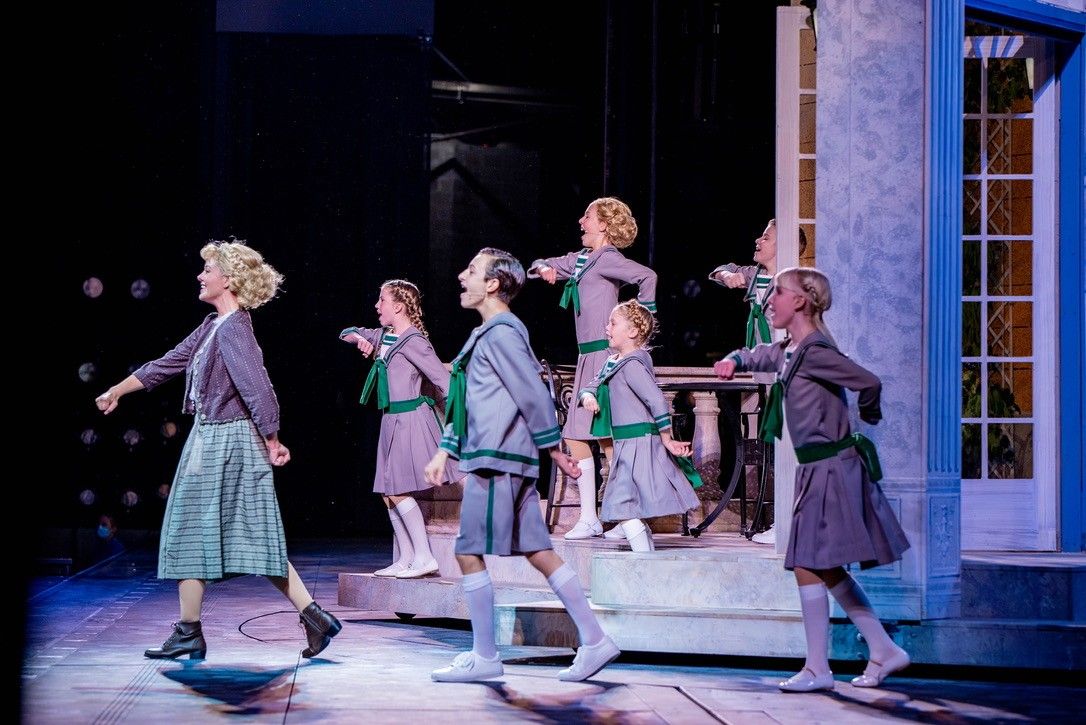 The von Trapp children in gray and green sailor costumes dancing across the stage with their governess at The Muny