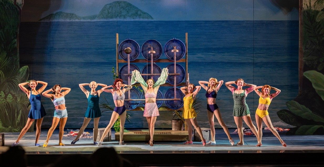 The company in 1940s swimwear posed in front of a painted ocean backdrop in South Pacific at The Muny