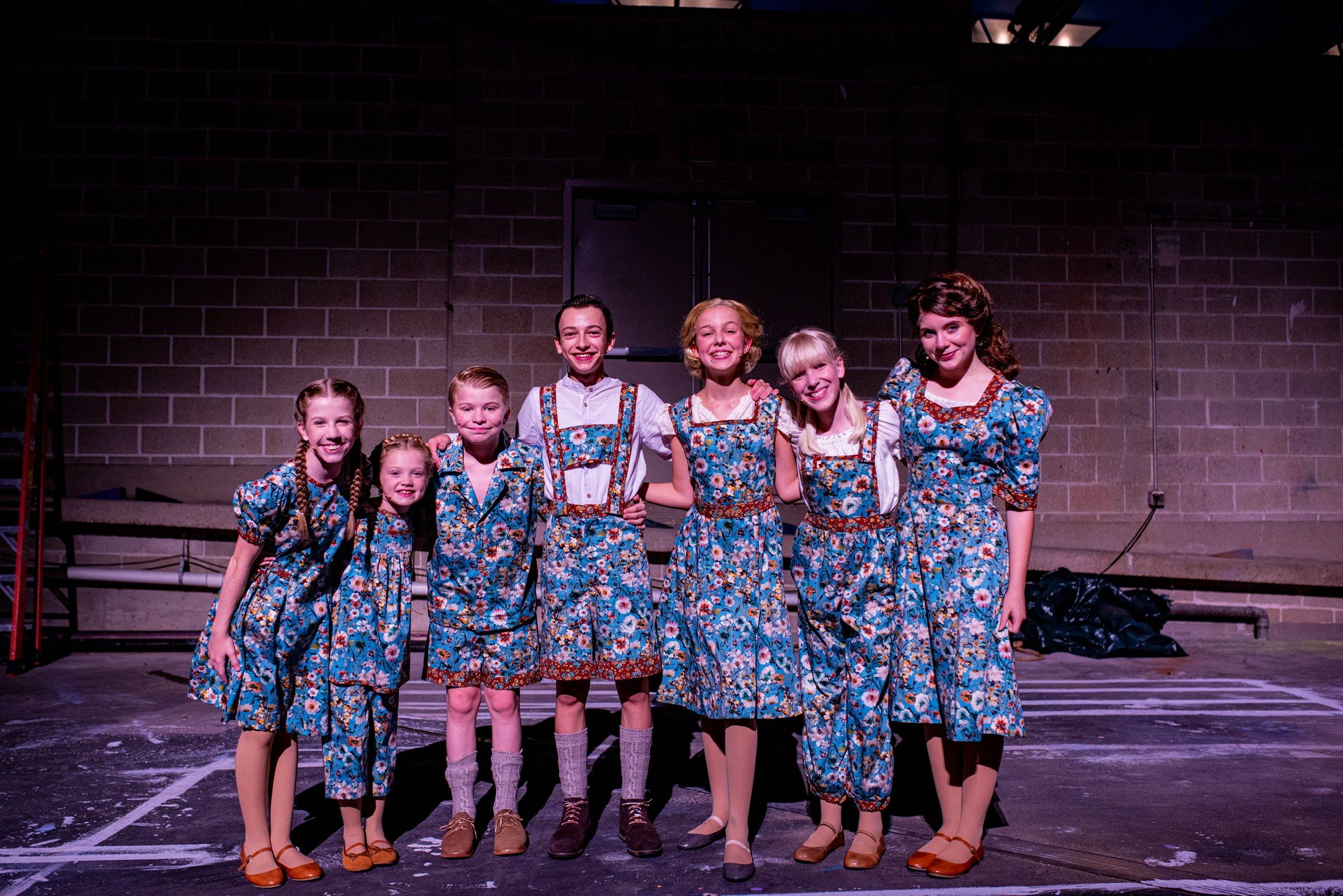 The von Trapp children in matching blue floral costumes on a dim stage at The Muny, Amelie Lock among them as Louisa